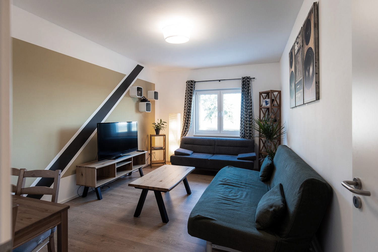 Lounge im Tonstudio mit gemütlichen Sofas, Fernseher, Pflanzen und moderner Küchenzeile.